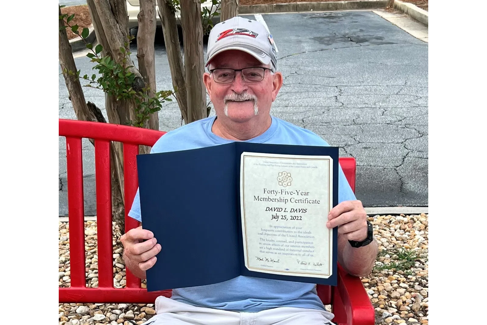 Daniel Davis sitting on a red bench holding a sign