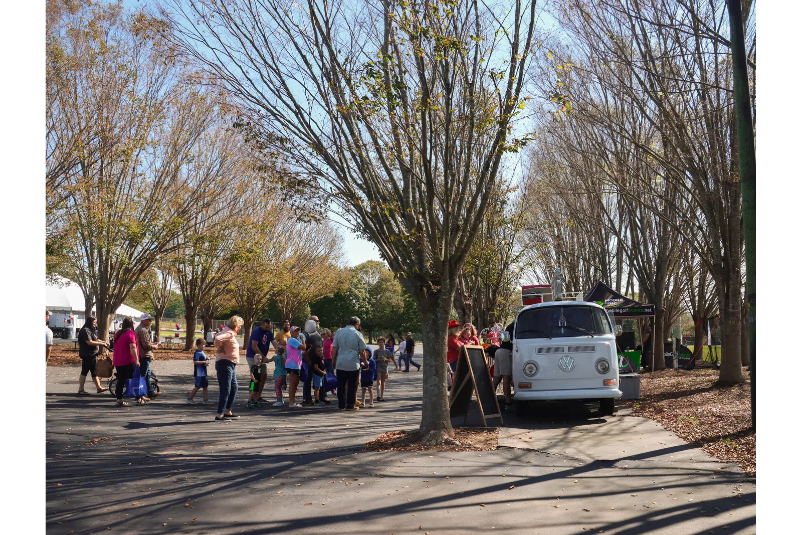 a group of people walking on a street with trees and a van
