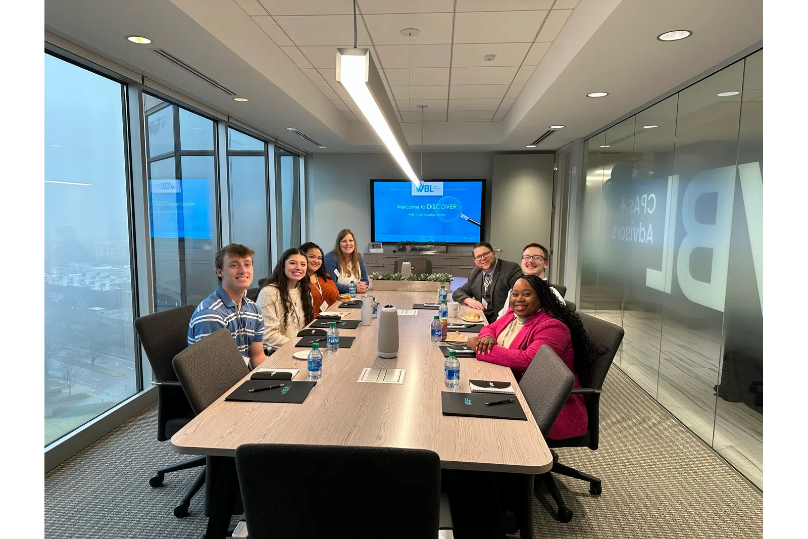 a group of people sitting around a table with a screen behind them