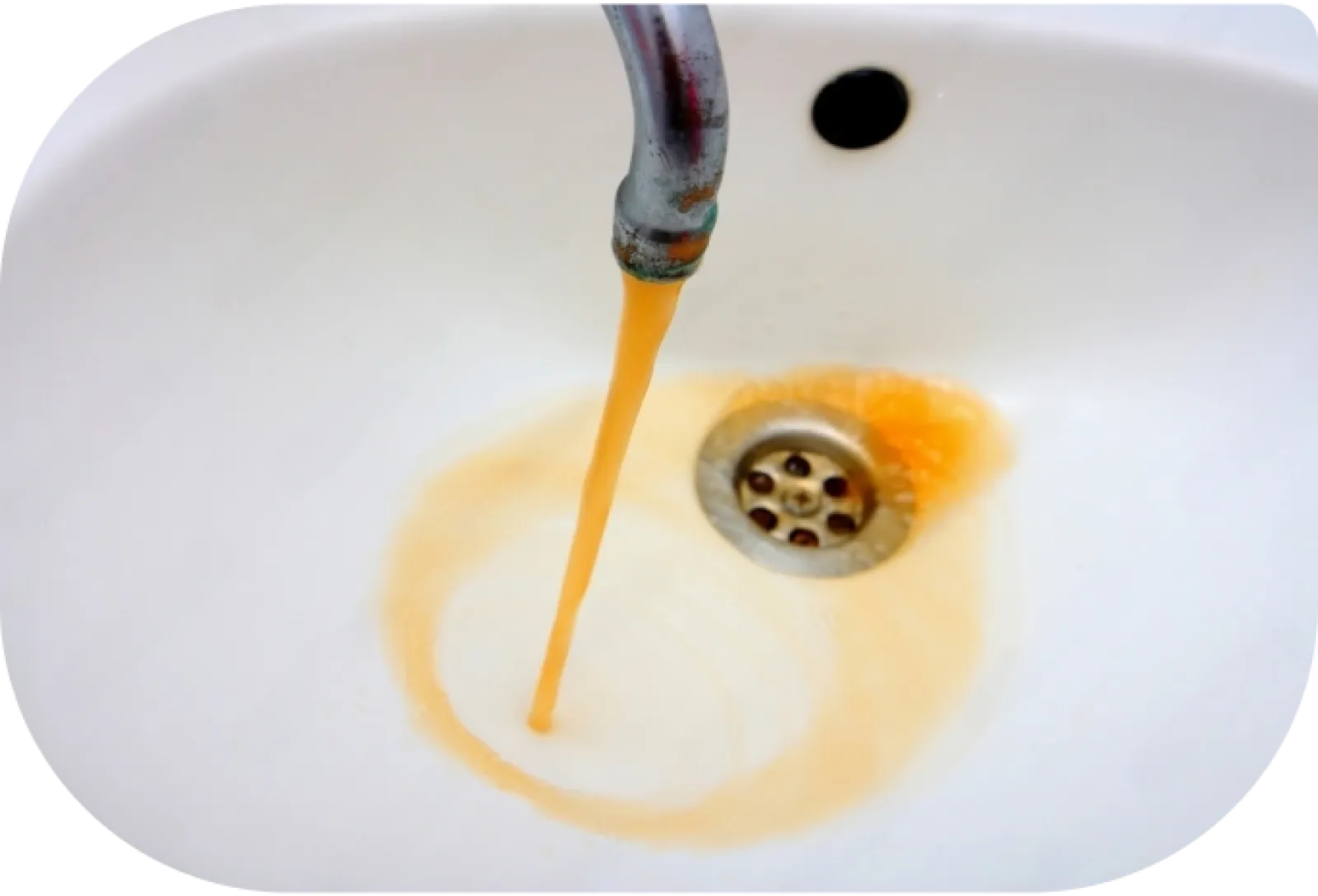 Rusty water flowing from faucet into white sink causing orange discoloration and staining around drain.