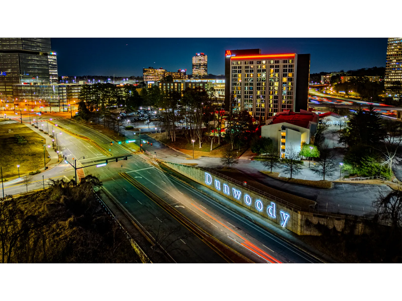 Night cityscape of Dunwoody with illuminated buildings and roads showing light trails from vehicles