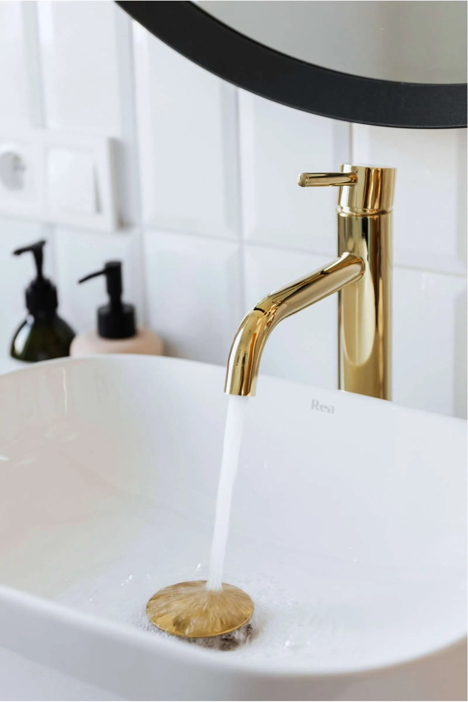 Modern bathroom sink with gold faucet running water into a white basin under a round mirror.