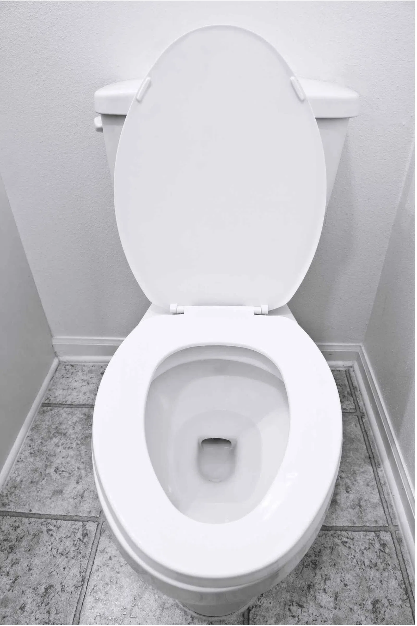 Top view of a clean white toilet with the lid open in a tiled bathroom corner.