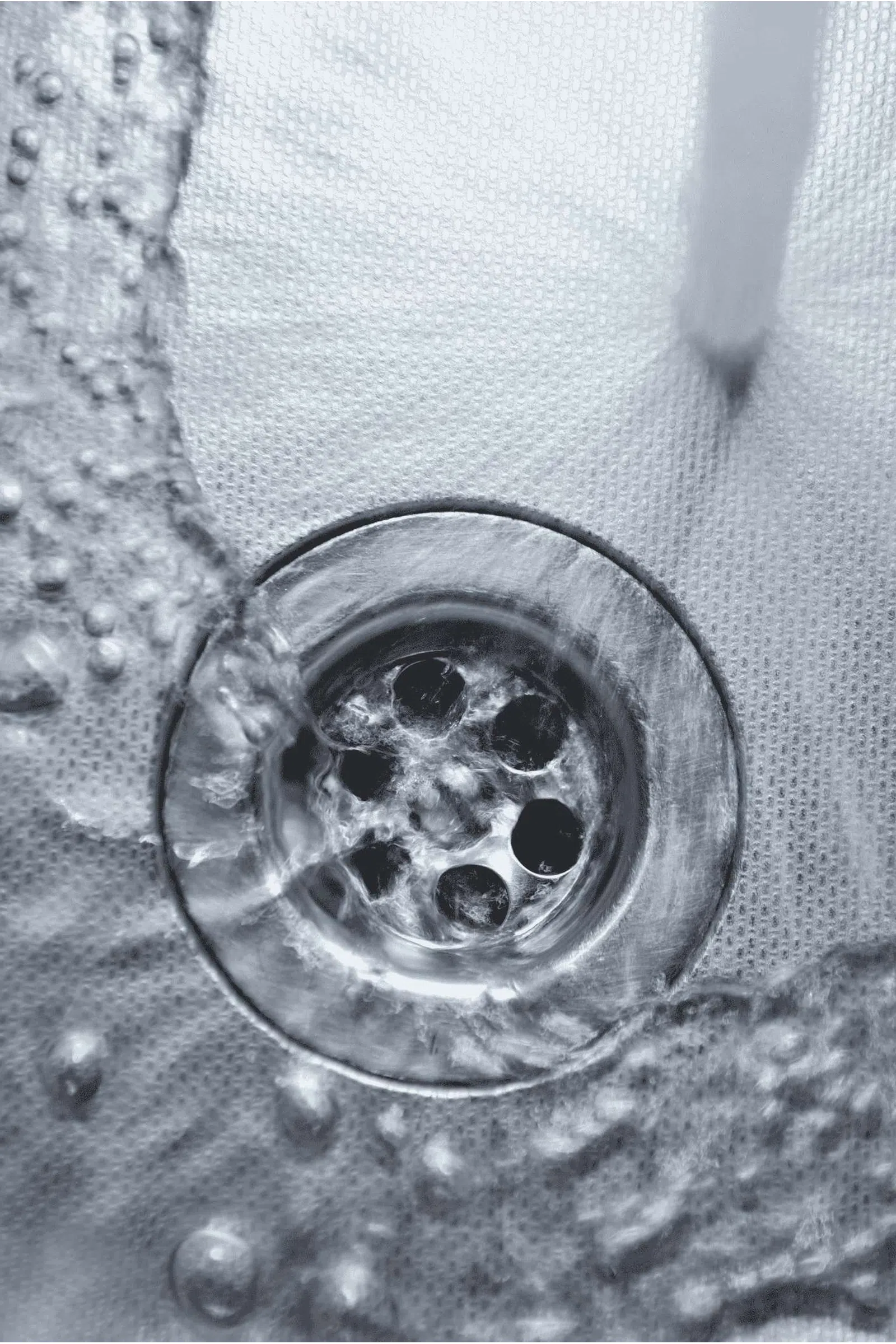 Close-up of clear water flowing into a metal sink drain with water bubbles and texture.