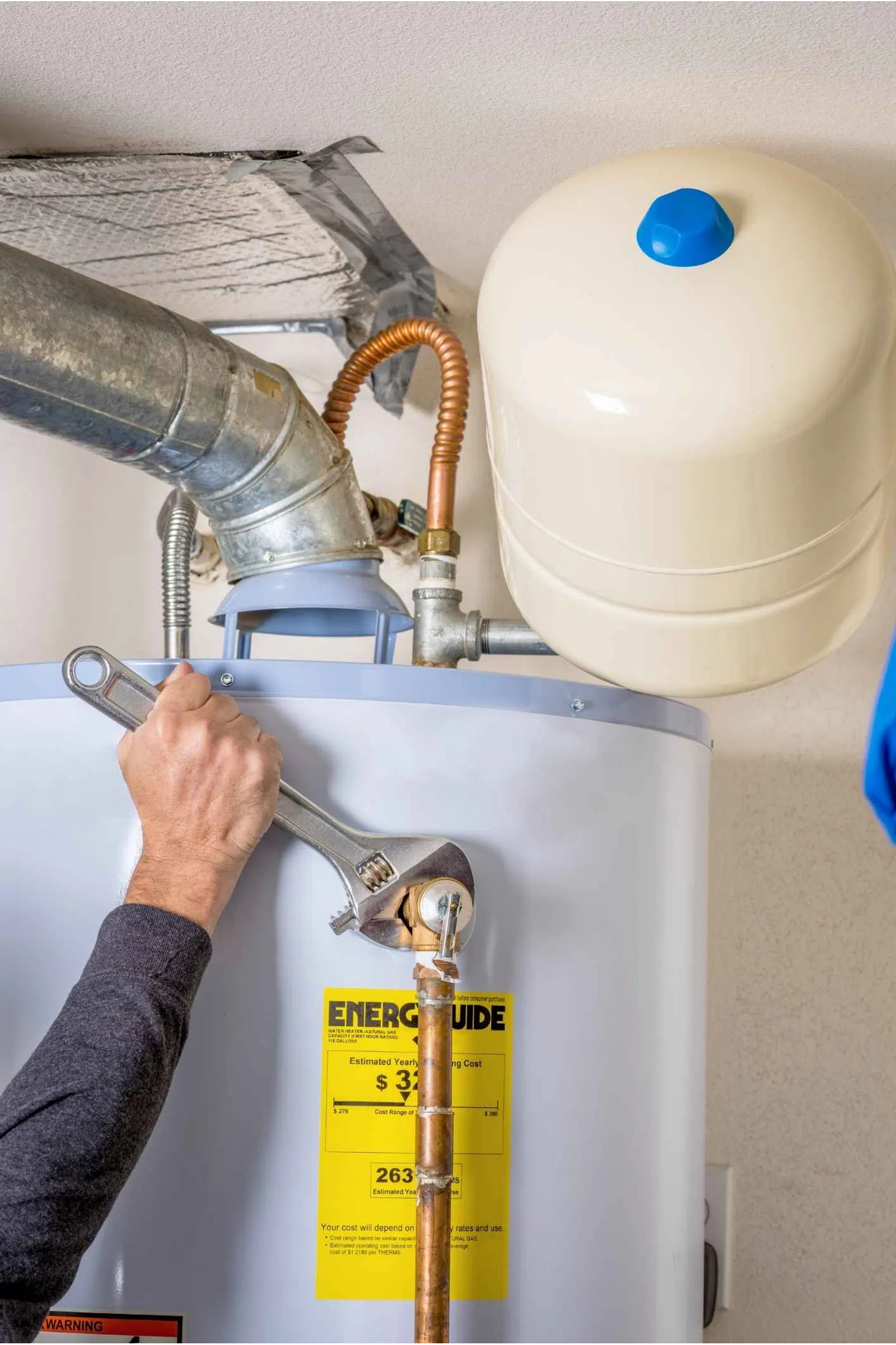 Plumber using a wrench to adjust pipes on a residential water heater with an energy guide label.