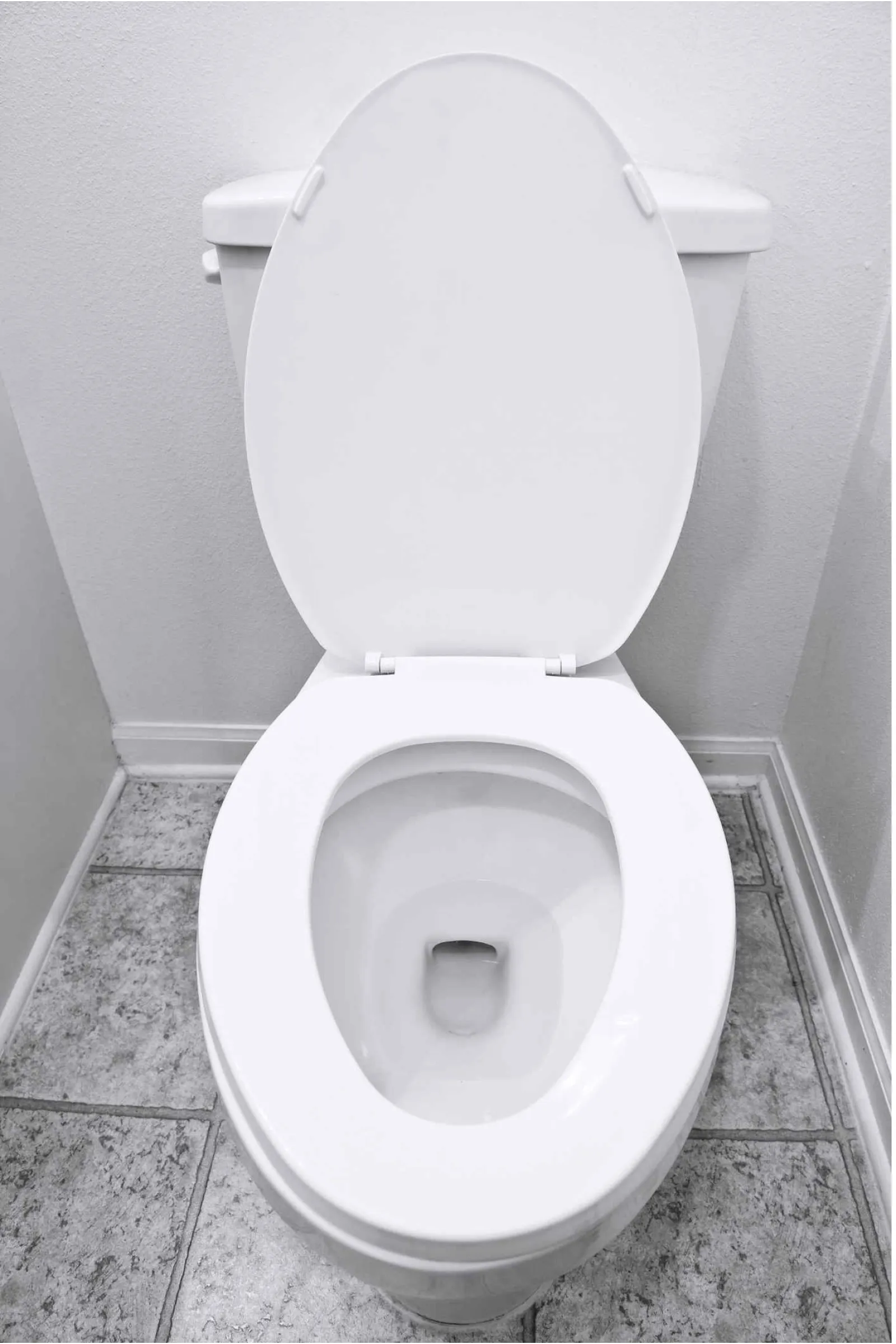 White ceramic toilet with open lid installed against a light gray wall on tiled floor.