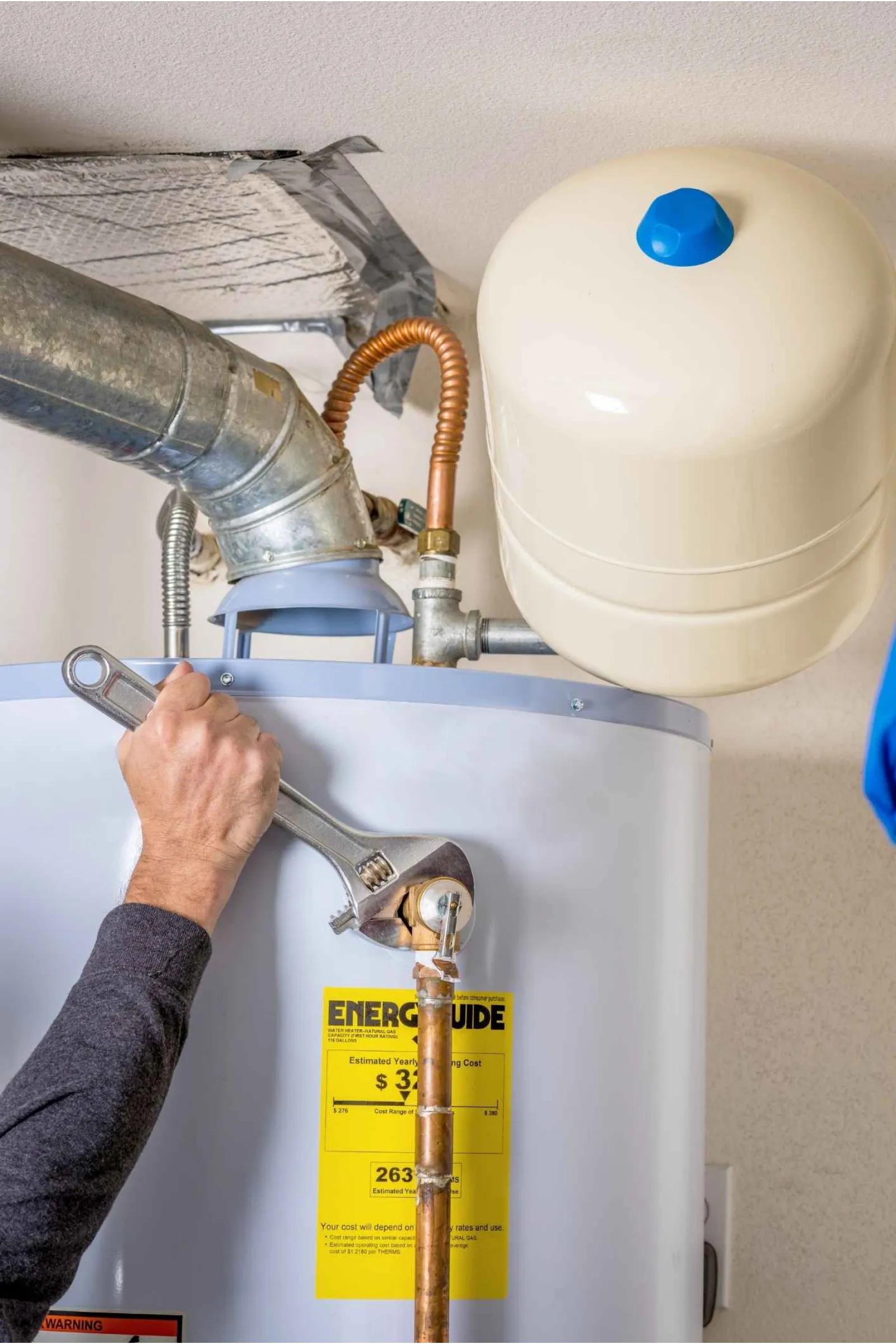 Technician uses a wrench to tighten a valve on a residential water heater with EnergyGuide label.