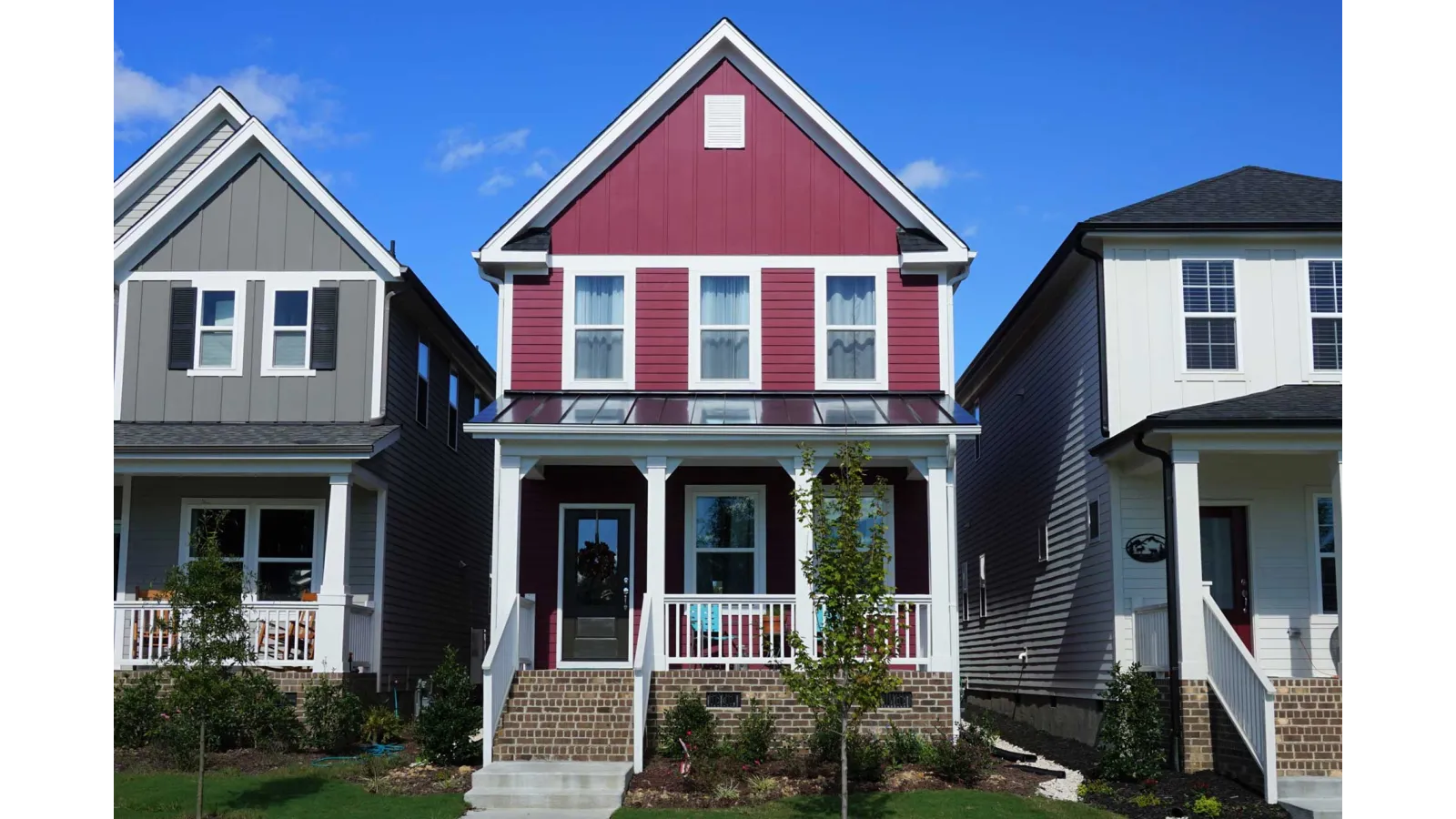 Front view of a red two-story house with white trim and brick steps under a clear blue sky