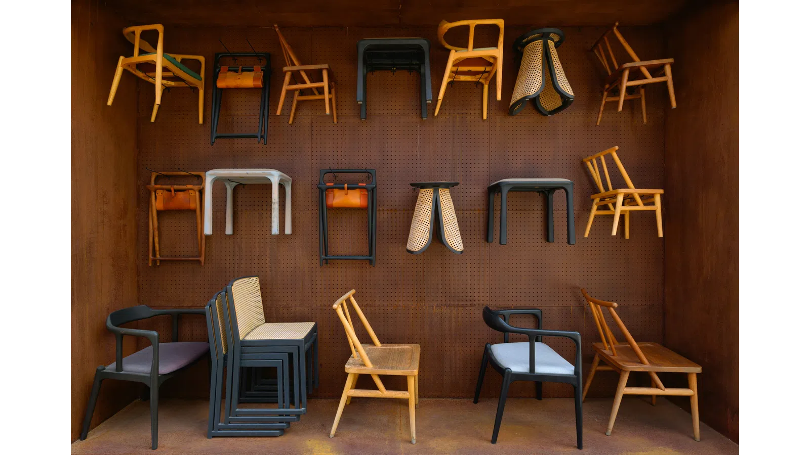Wooden and metal chairs displayed on and hanging from a perforated brown wall in a showroom.