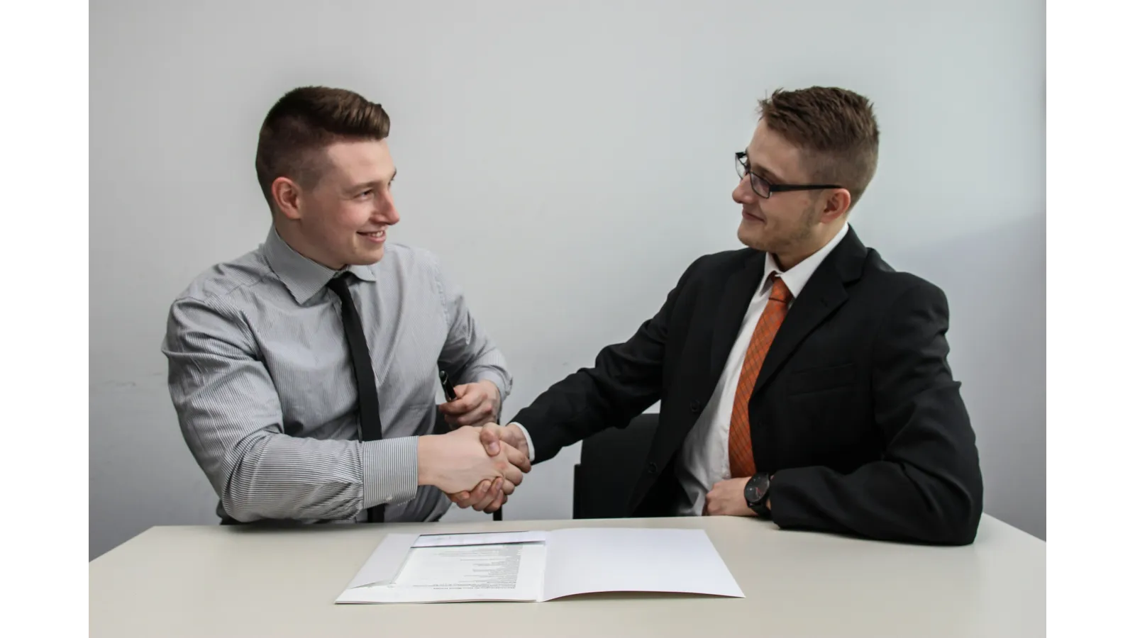 Two businessmen shaking hands over a desk with documents, symbolizing agreement or partnership.