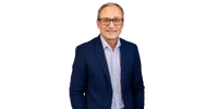 Smiling middle-aged man wearing glasses, a light blue shirt, and a navy blazer against a transparent background