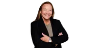 Smiling middle-aged woman with long hair wearing a black blazer and wristwatch against a black background