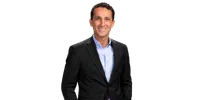 Smiling man in black suit jacket and light blue shirt posing against a plain background.