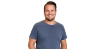 Smiling man with short hair wearing a blue t-shirt standing against a plain background.