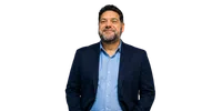 Smiling middle-aged man with beard wearing a blue shirt and navy blazer on black background.
