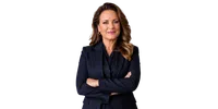 Confident businesswoman with crossed arms wearing a navy blazer and gold hoop earrings smiling at camera.