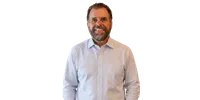 Middle-aged man with beard smiling, wearing light blue striped dress shirt against white background