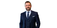 Smiling man in a navy blue suit with a tie and pocket square on a transparent background.