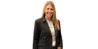 Smiling woman with long blonde hair wearing a black blazer and light shirt with badge around neck.