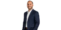 Smiling man in a navy blue suit and white shirt posing with one hand in pocket against a transparent background