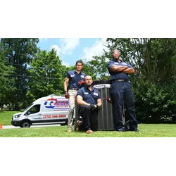 Three HVAC technicians posing outdoors by an air conditioner unit with a company van in the background showing we have HVAC service in your area.