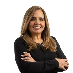 Confident middle-aged woman with brown hair smiling, wearing black sweater, arms crossed against white background