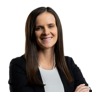 Professional woman with long brown hair wearing black blazer and white blouse smiling against white background