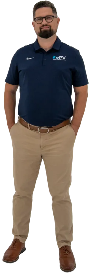 Man wearing navy blue polo with PV logo, khaki pants, brown belt, brown shoes, and glasses standing with hands in pockets.
