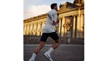 Man running outdoors near historical building in athletic wear during sunset with earbuds in ears