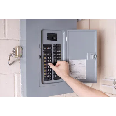 Hand adjusting a circuit breaker switch inside a gray electrical panel mounted on a wall with wiring.