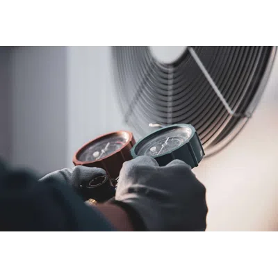 Technician using gauges to measure air pressure near an HVAC fan unit wearing protective gloves.