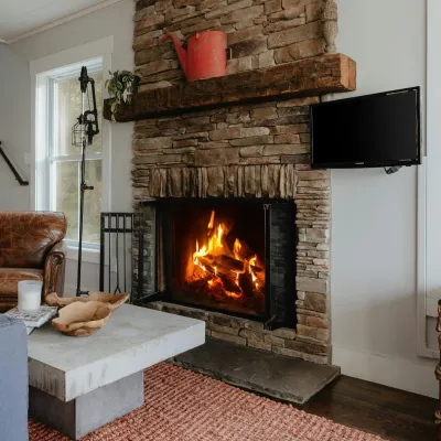 Cozy living room with stone fireplace, burning fire, leather armchair, modern sofa, and rustic decor