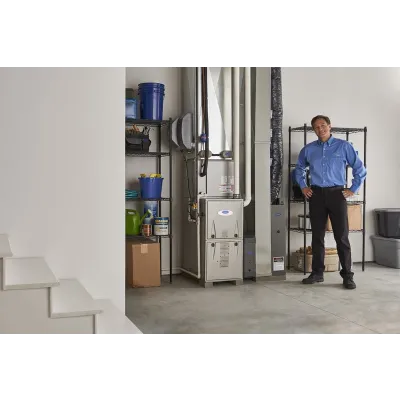 Technician in blue shirt standing beside modern furnace and organized storage shelves in a clean basement