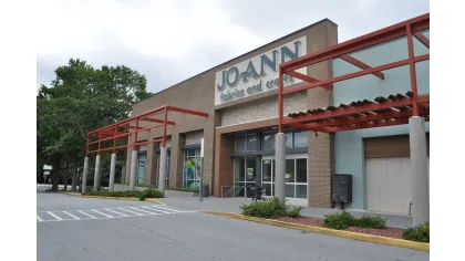 Exterior view of JOANN fabrics and crafts store with brick facade and red pergola on a cloudy day
