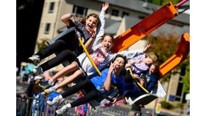 Children joyfully riding an outdoor amusement park swing ride on a sunny day with raised hands and smiles