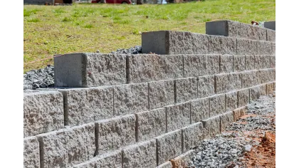 Construction of a tiered retaining wall with concrete blocks on a grassy slope with gravel base and red soil.