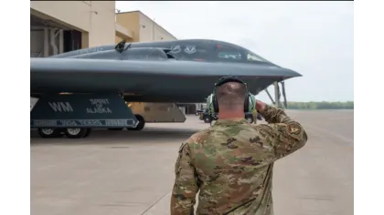 Military personnel saluting a B-2 Spirit stealth bomber on an airbase tarmac under clear sky