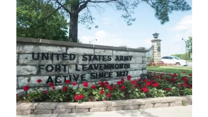 Stone sign at United States Army Fort Leavenworth entrance with red flowers and trees in background.