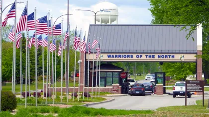 Entrance gate with American flags and sign reading Warriors of the North at a military base checkpoint.
