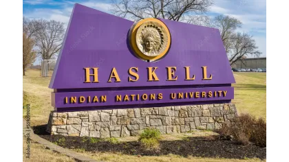 Purple and gold Haskell Indian Nations University sign with a stone base and Native American emblem outdoors.