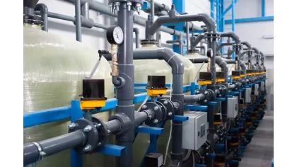 Industrial water filtration system with pipes, valves, pressure gauges, and large cylindrical tanks in a plant facility.
