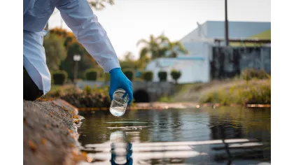 Scientist wearing blue gloves collects water sample from a river for environmental testing outdoors.