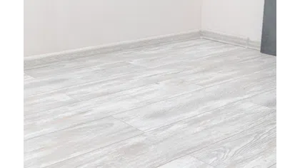 Light gray wood texture laminate flooring installed in a room corner with white walls.