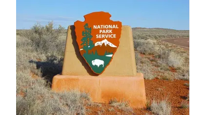 National Park Service sign with arrowhead shape, trees, mountains, and bison in a desert landscape