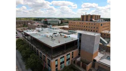 Aerial view of a multi-story brick building with a large rooftop under construction in a cityscape.