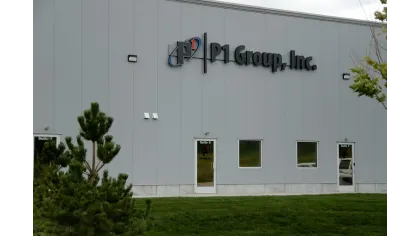 Exterior view of P1 Group, Inc. building with gray walls, company logo, green lawn, and trees in front