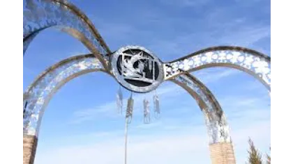 Decorative metal archway with circular emblem and intricate patterns against a blue sky background.