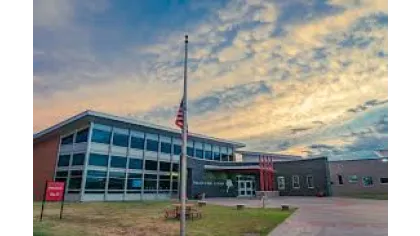 Modern school building with large windows, American flag at half-staff, and a vibrant sunset sky.