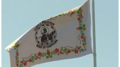 White Turtle Mountain Band of Chippewa flag with floral patterns waving against a clear blue sky.