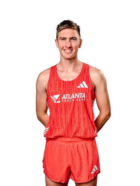 Smiling male runner wearing red Atlanta Track Club uniform with Adidas logos on tank top and shorts.